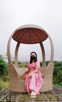 Portrait of woman wearing mask while sitting on chair against sky