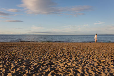 Woman standing on beach against sky during sunset