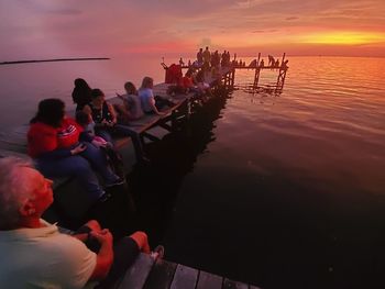 People sitting on boat in sea against sky during sunset