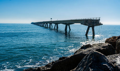 Pier over sea against clear blue sky