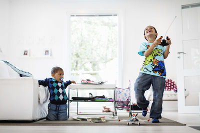 Boy looking at happy brother holding remote of model airplane at home