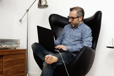 Man working on laptop having a relaxed coffee on the armchair at home