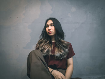 Portrait of young woman standing against wall