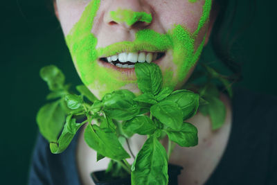 Close-up midsection of woman with face paint eating basil leaf