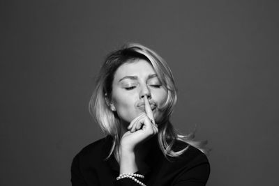 Young woman with finger on lips against gray background