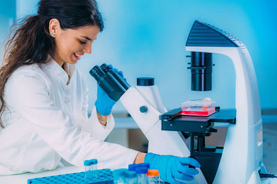 Female student in laboratory, placing culture flask on the microscope observation stage