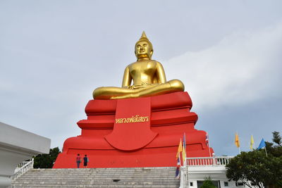 Low angle view of gold buddha statue against sky