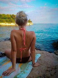 Rear view of woman looking at sea while sitting on beach towel