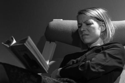 Tensed mid adult woman reading book while sitting on chair at home