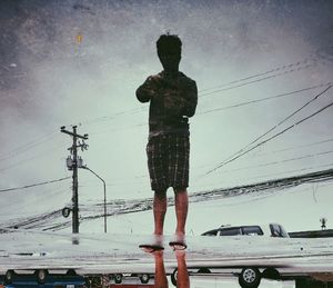 Man standing by electricity pylon against sky during winter