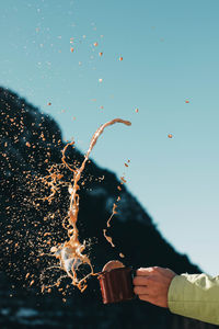 Cropped hand of man splashing drink against sky