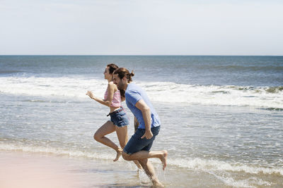 Side view of couple running on shore at beach during summer vacation