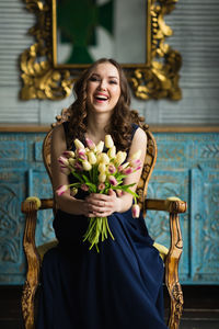 Portrait of young woman laughing while holding flowers on chair