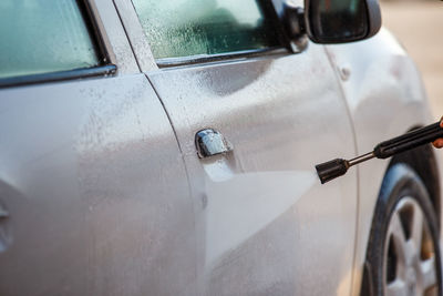 Hand with high pressure washer washing white car at public self service car washing station