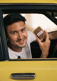 Portrait of young man showing food while sitting in car
