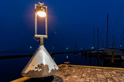 Close-up of illuminated light on pier by sea against blue sky