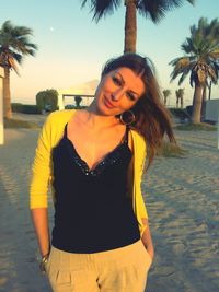 Portrait of beautiful young woman standing against palm trees