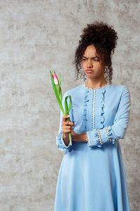 Young woman holding tulip while standing against wall