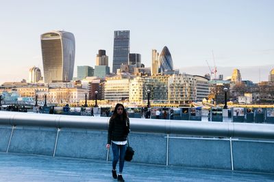 Woman walking on footpath against cityscape