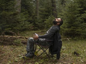 Side view of man sitting on chair in forest