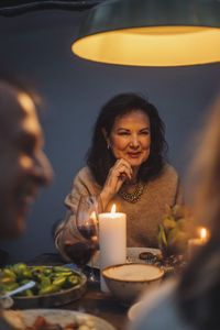 Smiling senior woman with hand on chin at illuminated dinner party