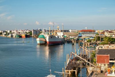 Sailboats moored in harbor by buildings against sky