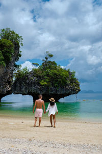 Rear view of woman walking on beach against sky