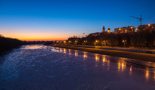 River by illuminated road against sky at night