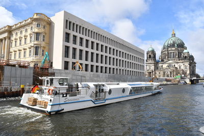 Boats in canal by buildings against sky in city