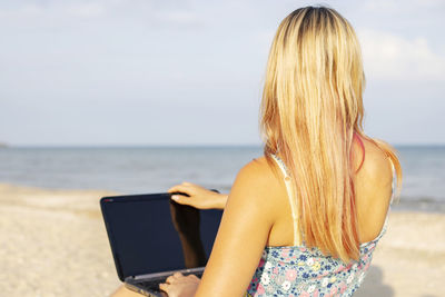 Rear view of woman using mobile phone at beach