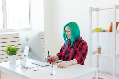 Portrait of young woman using phone while sitting on table