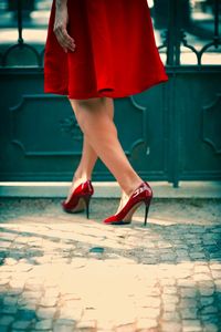 Low section of woman wearing red high heels while walking on footpath