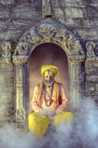 Sadhu sitting amidst smoke against built structure