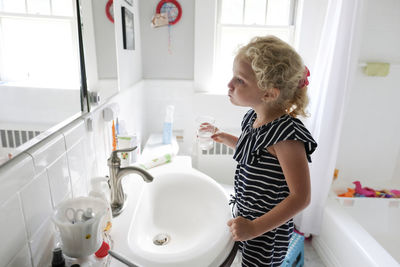 Side view of girl washing mouth while looking into mirror in bathroom