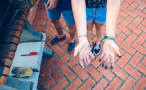 Low section of young woman showing dirty hands while standing on footpath