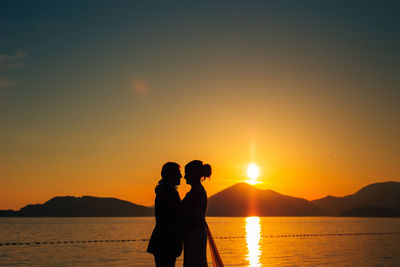 Silhouette couple standing against orange sky during sunset