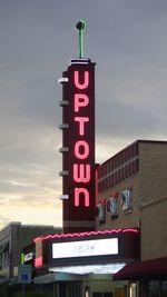 Information sign by illuminated building against sky