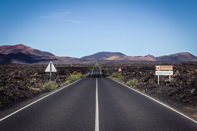 Road leading towards mountains against clear sky