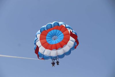 Low angle view of people paragliding against clear blue sky