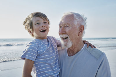 Happy grandfather carrying grandson on the beach