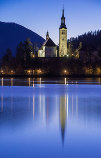 Illuminated church by lake against clear blue sky at night
