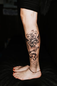 Unrecognizable female with pedicure and stylish two headed rat tattoo on leg standing in dark salon