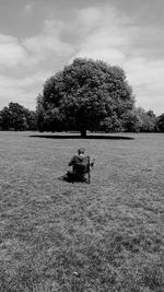 Man sitting on chair in field against sky