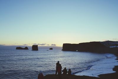 Silhouette people on beach against clear sky at sunset