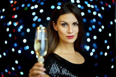 Portrait of beautiful woman having champagne against illuminated lighting equipment