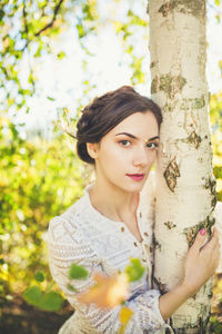 Portrait of young woman standing against birch tree trunk
