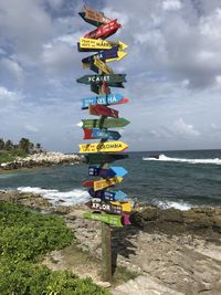 Colorful information signs at beach against cloudy sky