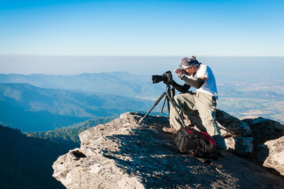 Full length of man photographing while sitting at cliff against landscape