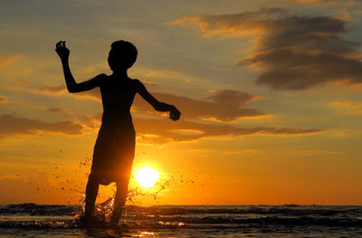 Low angle view of silhouette boy splashing water in sea