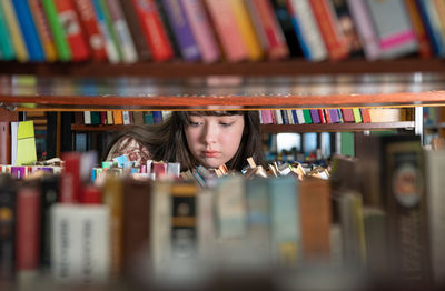 Girl standing between bookshelves in university library, picking up book from shelf. 